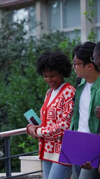 Vertical. Diverse group of students walk down campus steps after class, chatting and smiling with books and backpacks. Casual university scene showing friendship, teamwork and youthful energy.