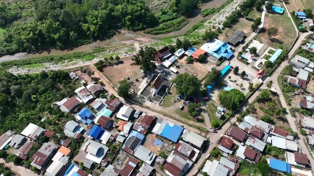 Wat Sri Kaew ordination hall in Nong Bua Lamphu, Thailand, surrounded by village houses, lush trees, and a riverside community in Nov 2023.