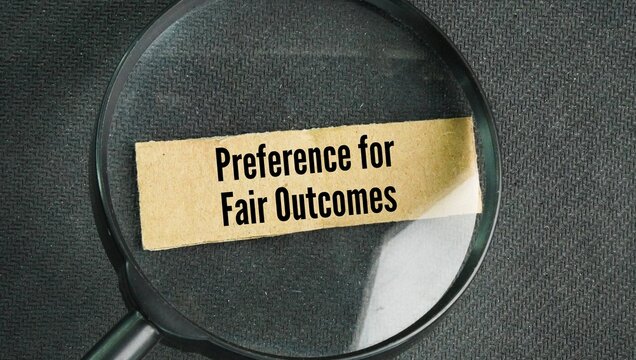 Magnifying glass with the words Preference for Fair Outcomes. Individuals value equity, balance, and the fair distribution of rewards or costs above their own self-interest.