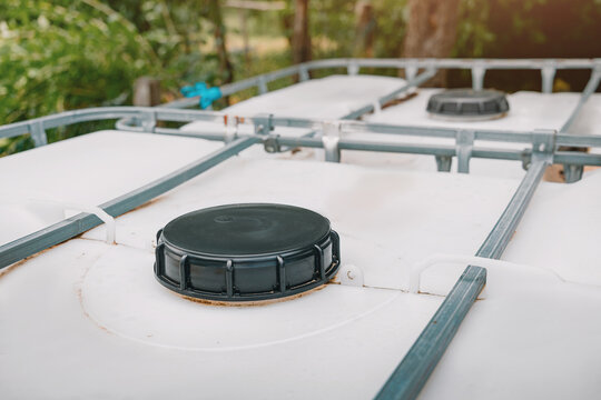 Close-up of plastic IBC tote tank lids and metal cage frame outdoors, used for bulk liquid storage and water collection. Agriculture concept.