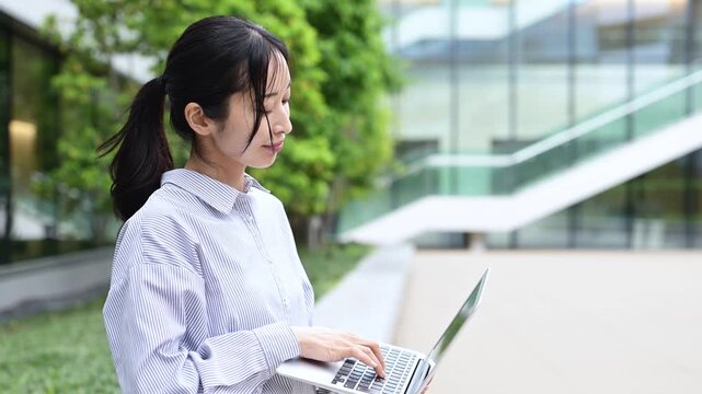 オフィス街でノートパソコンを使って仕事をする30代の日本人ビジネスパーソンの女性