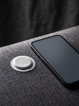 Minimalist smart tracker tag and smartphone on grey fabric surface, wireless tracking device for finding lost items, modern bluetooth locator technology for personal security
