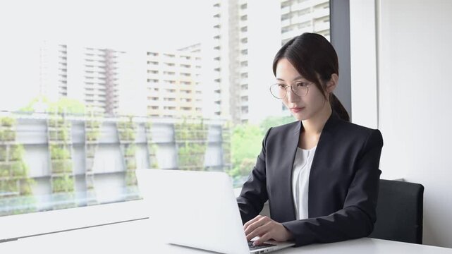 ノートパソコンを使って仕事をする眼鏡姿の20代日本人女性