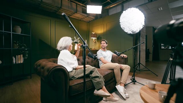 Man interviewing senior woman for podcast in recording studio. Presenters having discussion in conversation for their social media channel