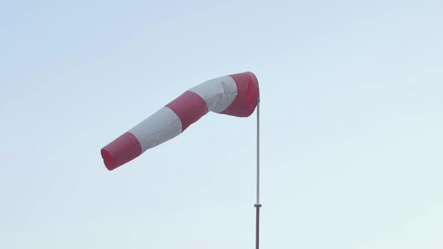 Red and white windsock blowing in the wind against sky background showing wind direction and speed