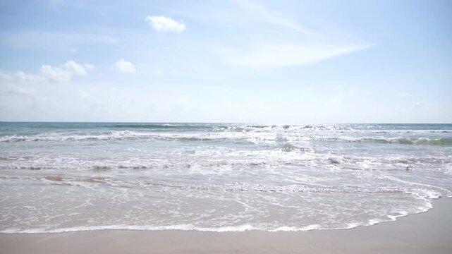 Gentle ocean waves rolling onto a sandy tropical beach under a bright blue sky with scattered clouds