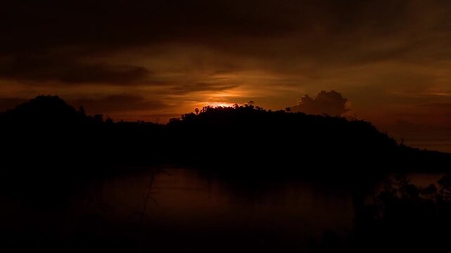 Time lapse captures a vibrant sunset over the Nagari Mandeh coast in West Sumatra. The bright yellow horizon transitions into deep red and dark hues as the sun dips below the ocean line. 