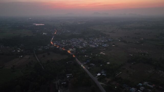 Tiny street lights and house lamps glow brightly across a quiet rural village in Nong Bua Lamphu during dusk.