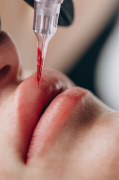 Extreme close up of a permanent makeup artist performing a lip blush tattoo procedure with a PMU machine in a professional beauty salon.