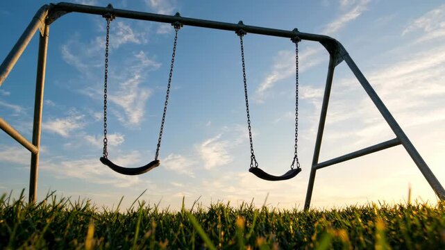 Two empty swings on a playground at sunset, symbolizing childhood and nostalgia.
