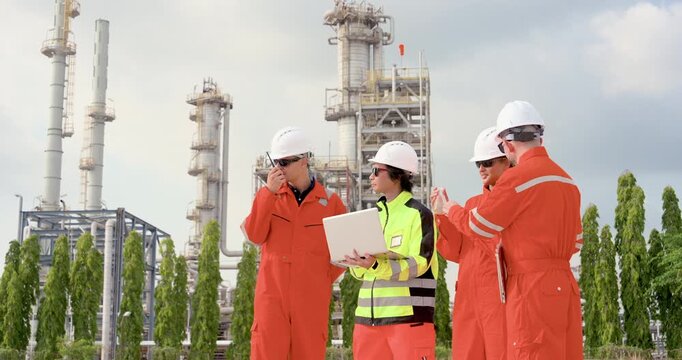 Multiracial refinery team communicates during safety briefing near processing tower, reviewing laptop data, sample result, pipeline inspection route, maintenance compliance plan outdoors onsite