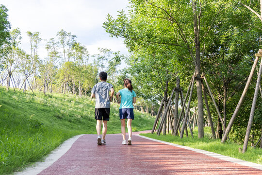 Two adult men and women jog side by side on a red paved path in a green, sunny park.