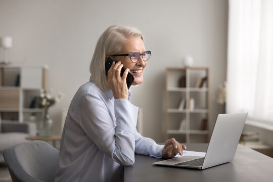 Senior woman finance advisor lawyer give professional phone consultation to client discuss business documents on laptop screen. Confident aged freelance specialist support customer on distance by cell