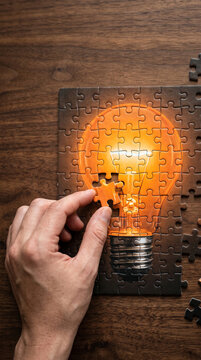 A jigsaw puzzle depicting a glowing lightbulb being completed, symbolizing the realization of ideas and innovation.