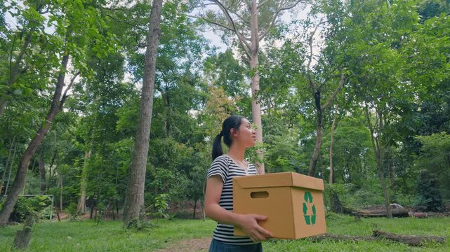 Asian woman holding recycling box on green nature forest background. Sustainable environment concept. Recycle plastic free of zero waste, from waste to environment.