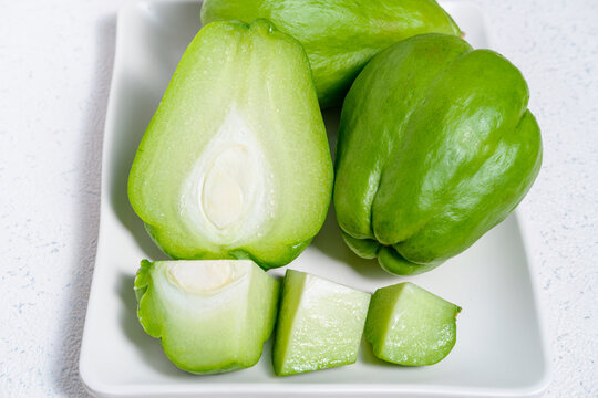 High angle shot of green chayote squash on a white square plate over a white surface.
