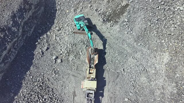 A large machine works in a granite quarry. The equipment digs into the ground, moving stones around the site. Workers manage the processes in the quarry to extract granite.