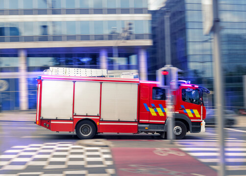 Fast Red firetruck rescue service fire brigade speeds through the city with emergency lights flashing, captured in a dynamic panning shot that highlights urgency, motion and urban emergency response.