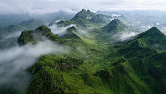 Aerial view of lush green mountain peaks covered in thick morning mist and clouds in a beautiful tropical landscape during the rainy season