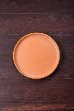 An empty round ceramic plate on a dark, textured brown background. An empty round plate