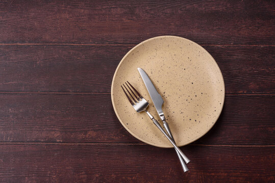 An empty round ceramic plate on a dark, textured brown background. An empty round plate