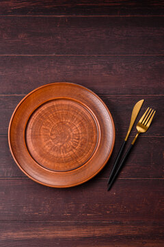 An empty round ceramic plate on a dark, textured brown background. An empty round plate