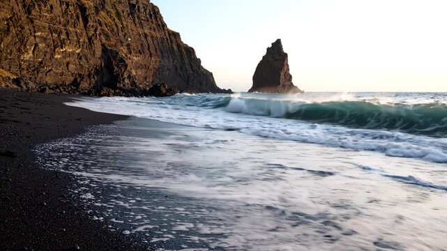 Waves washing over black sand beach at Reynisfjara, Iceland, with towering basalt sea stacks and cliffs at golden hour