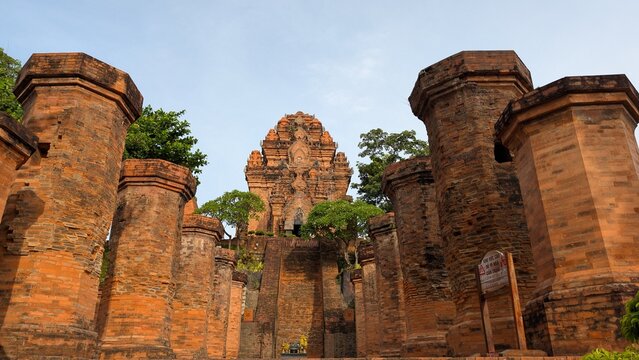 Historic Po Nagar Cham towers. The bottom of the picture shows an altar adorned with colorful religious offerings, framed by aligned brick columns. The composition highlights the intricate masonry.