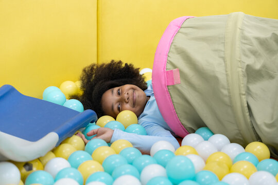 Smiling African American girl playing in ball pit tunnel