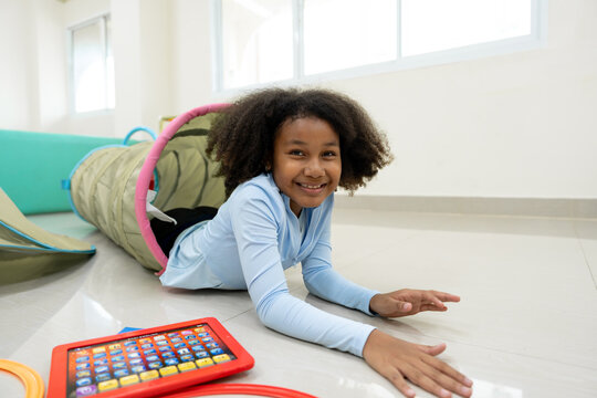 Smiling African American girl crawling through play tunnel in white room