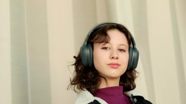 Calm teenage girl in big headphones disconnects from noise and problems, using favorite music to cope with anxiety and difficult emotions, theme emotional support for modern youth.
