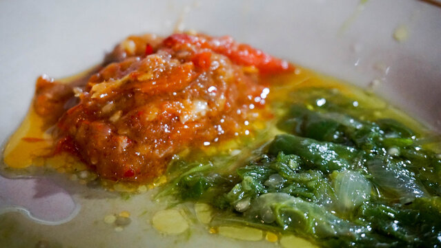Close up shot displaying red sambal and green sambal chili paste glistening with oil in a bowl, showing rich texture and vibrant colors.