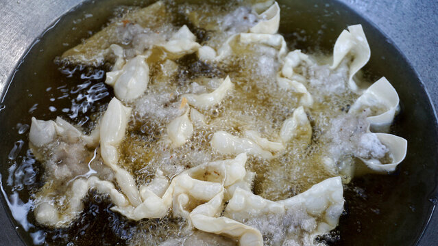 Detailed view of flour coated batagor dumplings deep frying in sizzling hot oil during cooking preparation.