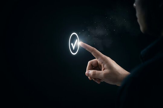 Person's finger touches a glowing checkmark icon on a dark digital interface.