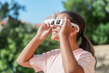 Obraz premium Smiling young woman wearing protective paper glasses to safely watch solar eclipse.