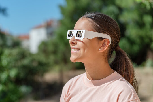 Smiling young woman wearing protective paper glasses to safely watch solar eclipse.