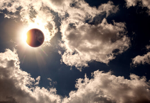 Solar eclipse with moon covering sun and dramatic cloud formations in sky.