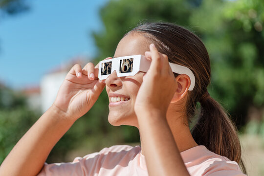 Smiling young woman wearing protective paper glasses to safely watch solar eclipse.