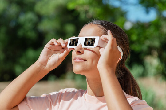 Smiling young woman wearing protective paper glasses to safely watch solar eclipse.