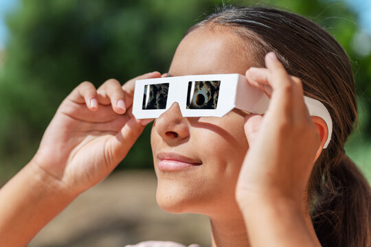 Smiling young woman wearing protective paper glasses to safely watch solar eclipse.