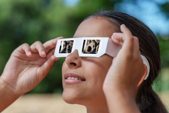 Smiling young woman wearing protective paper glasses to safely watch solar eclipse.