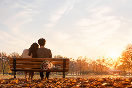 Rear view of couple on park bench with flowers and chocolates, autumn romance concept