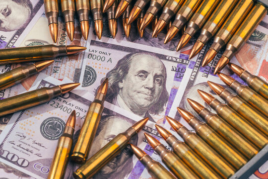 bullets over one hundred US dollar bills banknotes as a conceptual metaphor for global geopolitical conflict war finance military capitalism arms trade and budget defense with copy space.