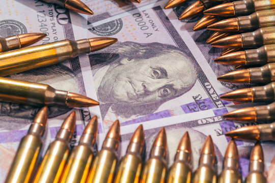 bullets over one hundred US dollar bills banknotes as a conceptual metaphor for global geopolitical conflict war finance military capitalism arms trade and budget defense with copy space.