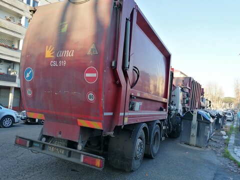 Rome, Italy - January 17, 2022, two AMA garbage trucks parked in single file in front of a set of garbage buckets.