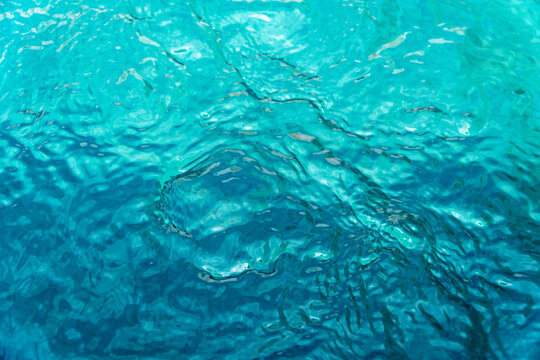 Vibrant turquoise water ripples texture background, looking down into a clear swimming pool or sea with light reflections and movement. Ideal for summer or travel concepts.