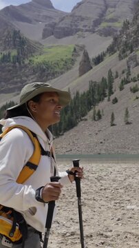 Vertical. Black woman hiking in a remote mountain landscape with lake and forest, evoking Yosemite or Banff, walking with trekking gear and enjoying peaceful natural surroundings