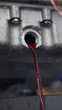 Detailed shot of red transmission oil flushing or draining out of a metal machinery component in a garage.