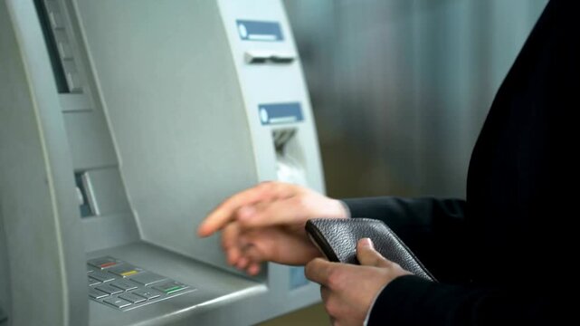 Business man inserting credit card in ATM machine keyboard and entering security pin code to receive money in 4K Ultra HD footage
