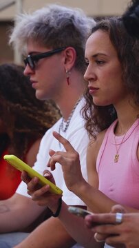 Two cheerful young women are sitting on outdoor stairs, enjoying some funny content on a smartphone, creating a joyful and connected moment